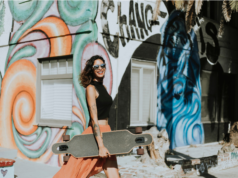 woman with tattoos is holding a longboard