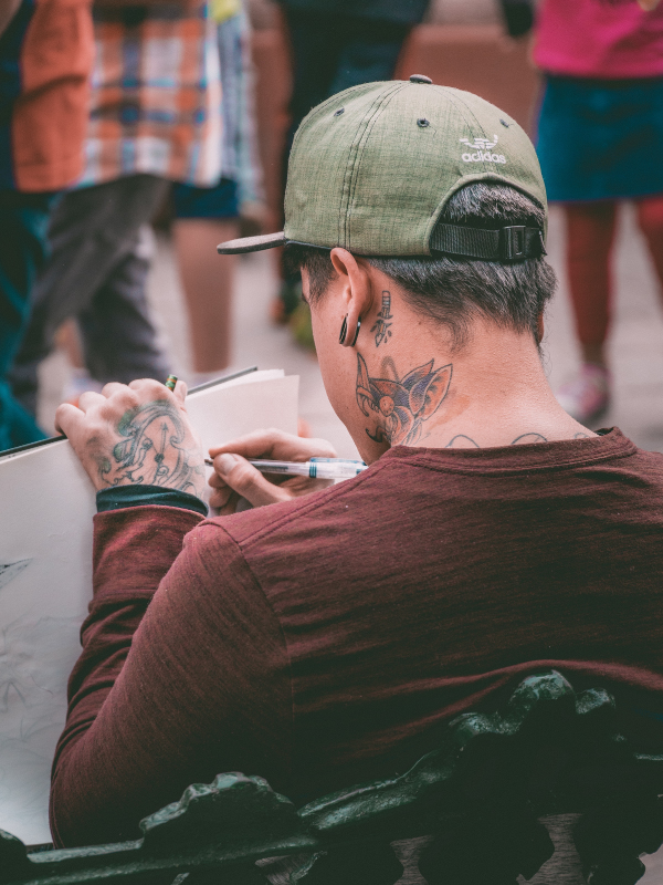 man with tattoo on his neck is writing in a notebook
