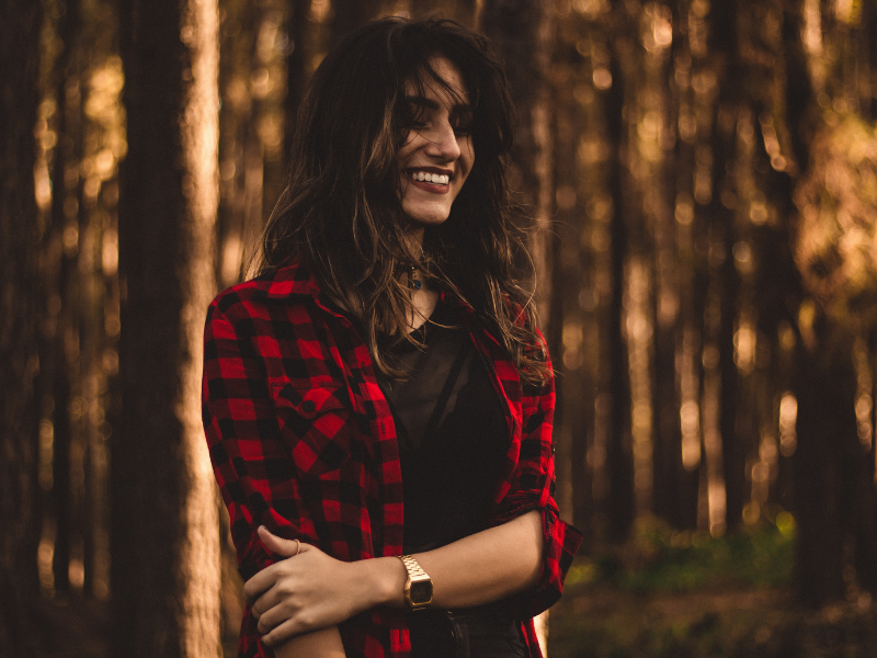 woman smiling in the woods wearing a flannel shirt
