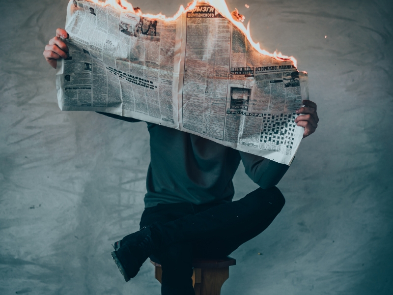 man sitting in a chair holds a burning newspaper