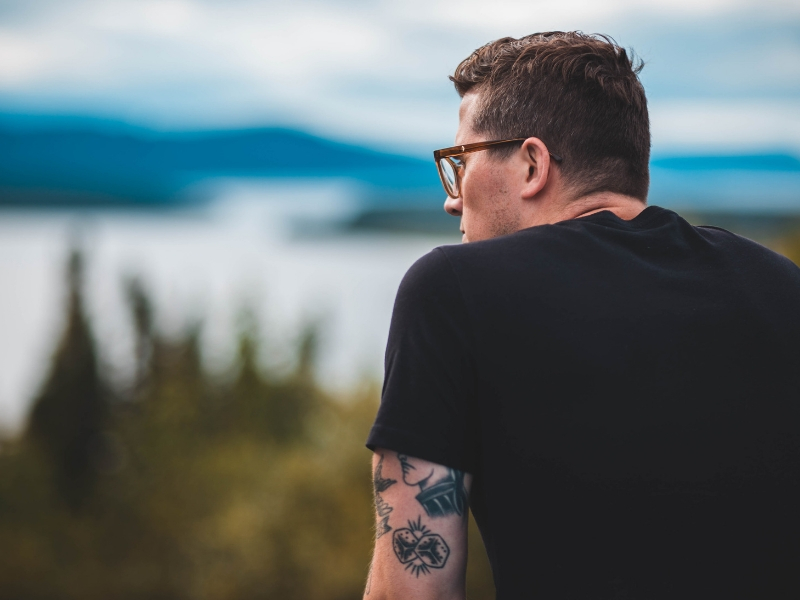 a man with tattoos looks out over a lake