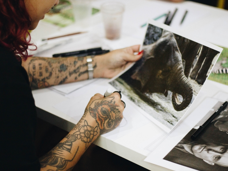 a woman with tattoos is sketching from a photograph