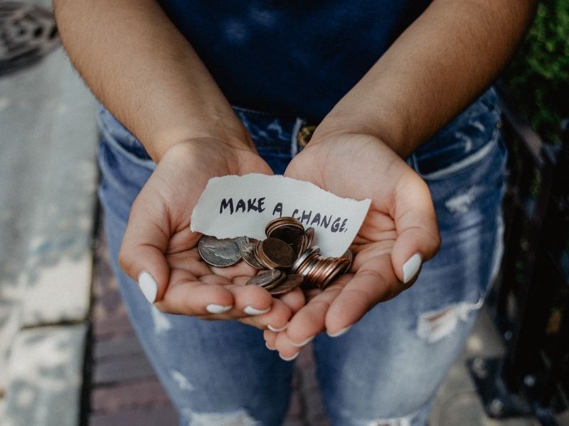 close up of two hands holding change and a sign saying _make a change