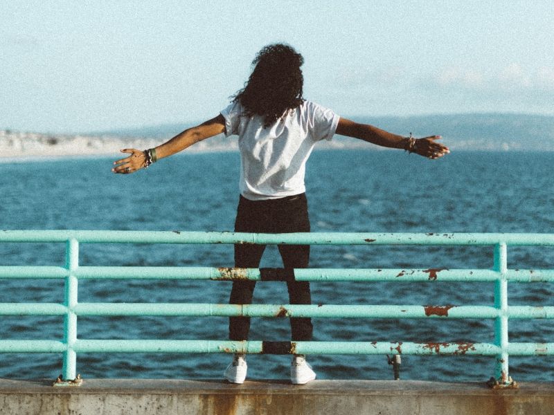 young woman standing by the ocean spreading her arms