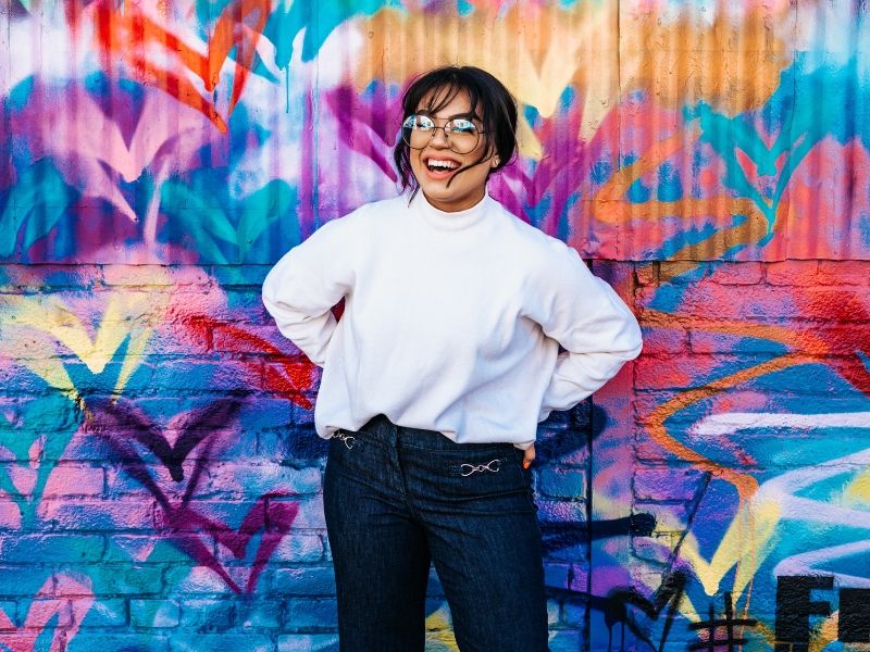 a young woman laughing in front of a graffiti covered wall