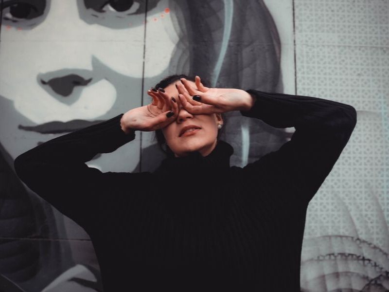 woman covers her eyes in front of a wall
